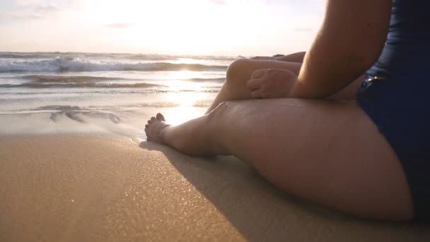 Красивая молодая женщина лежит на золотом песке на морском пляже и отдыхает во время летних каникул. Сексуальная девушка, сидящая на берегу океана и загорающая. Медленное движение Закрыть низкий угол обзора — стоковое видео