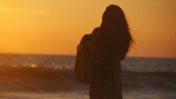 Una joven viajera irreconocible que va a la orilla del mar al amanecer. Joven turista con mochila caminando a lo largo de la playa al atardecer. Chica excursionista pisando durante los viajes o vacaciones. Movimiento lento — Vídeo de stock