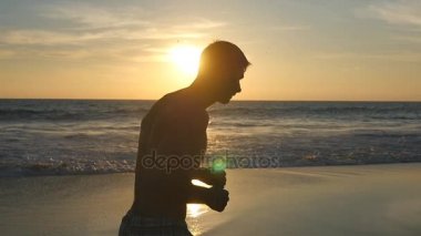 Atletik adam okyanus kıyı gündoğumu sırasında koşu. Deniz sahilde günbatımında çalışan sportif delikanlı. Açık egzersiz erkek sporcu. Sağlıklı aktif yaşam tarzı. Doğa, egzersiz. Ağır çekim