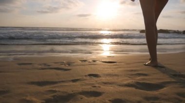 Günbatımında yıkanmak için deniz plajda mayolu genç kadın gider. Tatil sırasında okyanus kıyısında yürüyüş güzel genç kız. Yaz tatile dinlenmek. Arka geri görüntülemek ağır çekim