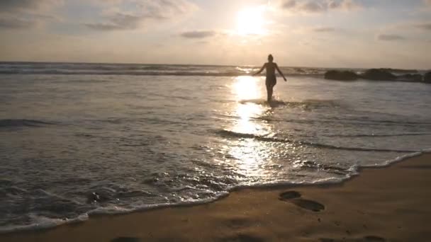Fürdőruha fiatal nő megy a tenger part naplementekor. Szép fiatal lány séta a parton az óceán, nyaralás alatt. Pihenjen a nyári szünet. Hátsó vissza Nézd lassú mozgás