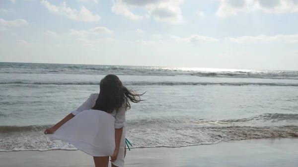 Donna felice in bikini e camicia che cammina sulla spiaggia all'acqua dell'oceano. Giovane bella ragazza godendo la vita e divertirsi sulla riva del mare. Vacanze estive o vacanze. Vista posteriore posteriore — Foto Stock