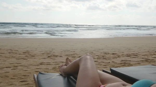年轻女子躺在海上和日晒日光浴浴床。女性的身体在放松和享受暑假期间在空的沙质海滩上的躺椅上。在度假村的比基尼的女孩。关闭 — 图库照片