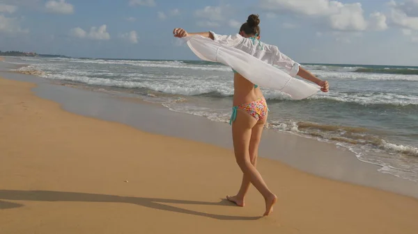 Mulher bonita em maiô e camisa andando na praia do mar descalça e levantou as mãos. Menina indo na costa do oceano e desfrutando de verão. Ondas marinhas ao fundo. Conceito de férias — Fotografia de Stock