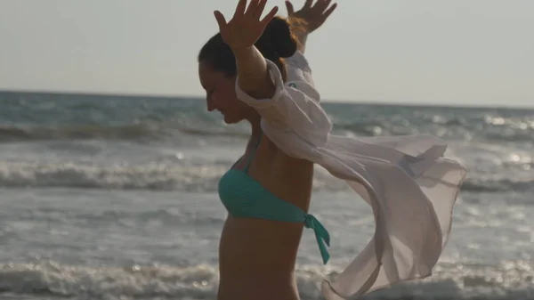 Lycklig kvinna i bikini och skjorta som promenerar på stranden nära havet och lyftta räcker. Ung vacker flicka njuter av livet och att ha kul på havet. Sommarsemester eller semester. Profil på nära håll se — Stockfoto