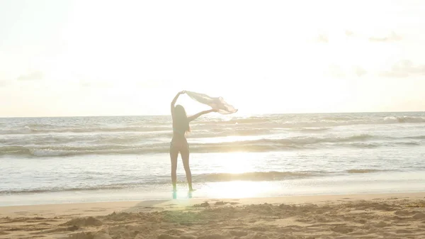 Młoda kobieta szczęśliwy szal uruchomiona na ocean plaża o zachodzie słońca. Dziewczynka korzystających lato. Kobieta w bikini z latania szalik w rękach jogging na brzegu morza. Z bliska — Zdjęcie stockowe