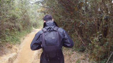 Seyahat sırasında ahşap parkurun gidiş yağmurluk genç adam. Sırt çantası tropikal ıslak ormanda yürüyüş yürüyüş adamla. Erkek turist orman yolunda adım için izleyin. Arka arkadan görünüm