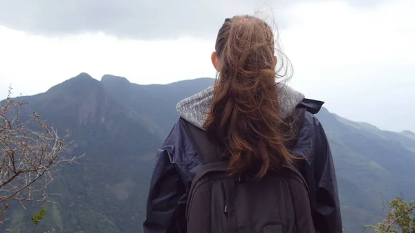 Güzel Kanyon kenarında duran ve manzara zevk tanınmaz halde kadın turist. Genç kadın uzun yürüyüşe çıkan kimse dağ ve yükseltilmiş elleri yukarı ulaşan sırt çantası ile yağmurluk içinde. Arka arkadan görünüm
