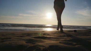 Kumsalda okyanusa günbatımında çalışan genç kadın. Güzel genç kız kıyıda denize tatil sırasında olacak. Yaz tatile dinlenmek. Arka geri görüntülemek ağır çekim
