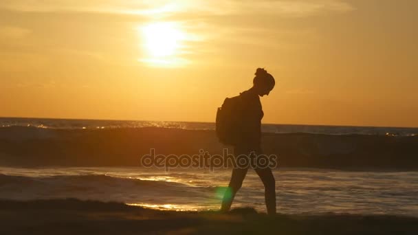 Joven turista con mochila caminando a lo largo de la playa al atardecer. Hermosa joven viajera que va a la orilla del mar al amanecer. Chica excursionista pisando durante los viajes o vacaciones de verano — Vídeos de Stock