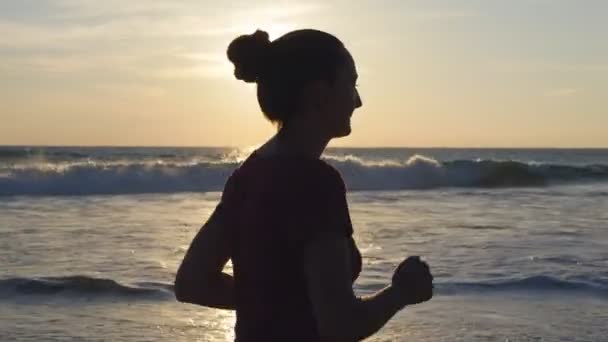 夕暮れ時の海のビーチで実行されている若い女性のシルエット。女の子の日の出時海海岸に沿ってジョギングします。屋外運動女性スポーツマン。自然で健康的なエクササイズのライフ スタイル。クローズ アップ — ストック動画