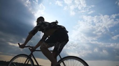 Genç adam arka plan güzel günbatımı gökyüzüne vintage bisiklet sürme silüeti. Sportif adam ülkede yol Bisiklete binme. Erkek bisikletçi binicilik bisiklet. Sağlıklı aktif yaşam tarzı ağır çekim