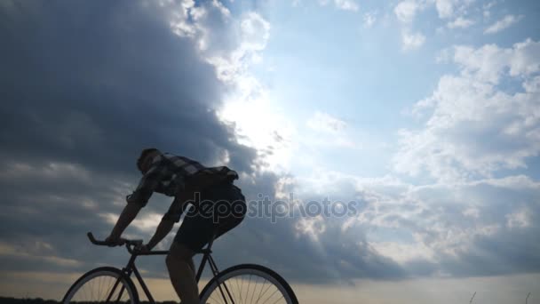 年轻男子骑在老式自行车与美丽的夕阳的天空背景下的剪影。在乡村的小路上骑自行车运动的家伙。踏单车的男子骑自行车。健康积极的生活方式慢动作 — 图库视频影像