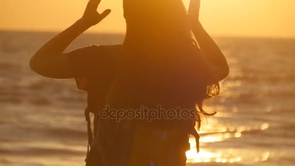 Giovane donna turistica che lega coda di cavallo sulla spiaggia vicino al mare al tramonto. Bella ragazza spremere i capelli sulla riva dell'oceano all'alba. Donna zaino in spalla treccia capelli e facendo acconciatura. Cura dei capelli Vista posteriore — Video Stock