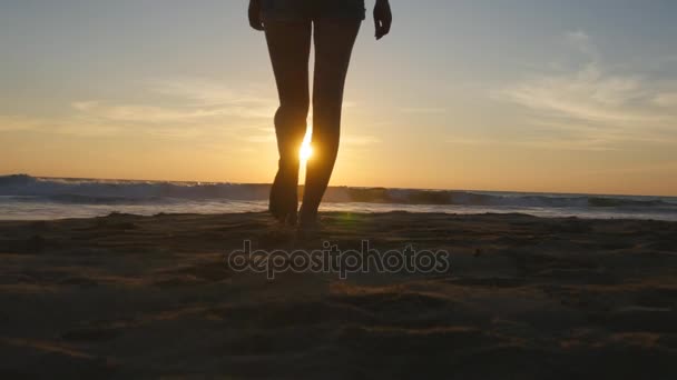 Young woman tourist with backpack walking on beach to the ocean at sunset and raised hands. Girl hiker going on sandy shore to the sea and enjoying freedom during summer vacation. Rear back view — Stock Video