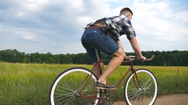 若い男が畑の上の田舎道でヴィンテージ自転車に乗っている。田舎のトレイルアウトドアに沿ってスポーティ男サイクリング。田舎で自転車に乗る男性サイクリスト。健康的なアクティブなライフスタイルスローモーション — ストック動画