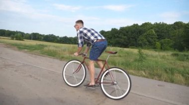 Ülkede yol Vintage Bisiklet sürme yakışıklı delikanlı. Sportif adam kırsal iz Bisiklete binme. Erkek bisikletçi sabit sürme karayolu Bisiklet dişli. Sağlıklı aktif yaşam tarzı ağır çekim