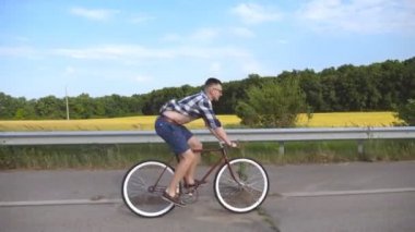 Kırsal yolda klasik bisiklete binen genç yakışıklı adam. Sportif adam pistte bisiklet sürüyor. Erkek bisikletçi otoyolda sabit vitesli bisiklet sürüyor. Sağlıklı aktif yaşam biçimi Kapat