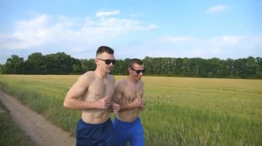 Çalışan ve açık havada konuşurken iki kaslı adam. Atletik çocuklar alanın üzerine koşu gülümseyen genç. Erkek sportsmans eğitim doğa birlikte. Dışarıda egzersiz arkadaşlar. Sağlıklı aktif yaşam tarzı