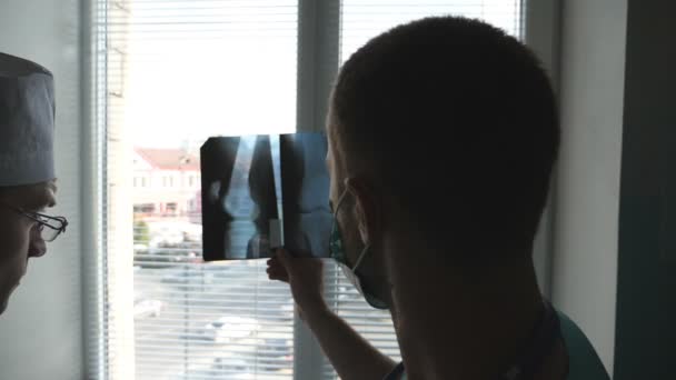 Két orvos Nézd a kép mri és beszélünk róla. Kórház egészségügyi dolgozók vizsgálata röntgen nyomatok. Férfi orvosok konzultálnak egymással, miközben nézte a röntgensugárzás kép. Lassú mozgás hátsó vissza Nézd — Stock videók