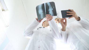 Hastanın röntgen görüntüsü hakkında birbirlerine danışırlarken tablet kullanan sağlık görevlileri. Hastanedeki tıp çalışanları röntgen izlerini inceliyor. Kafkasyalı iki doktor MRI fotoğrafına bakıp bunu tartışıyor.