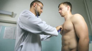 Doktor muayene genç erkek hasta stetoskop ile. Tıbbi işçi dinleme kalp atışı atletik adam. Göğüs Hastanesi ofisinde bir adam kontrol doktor. Yakın çekim