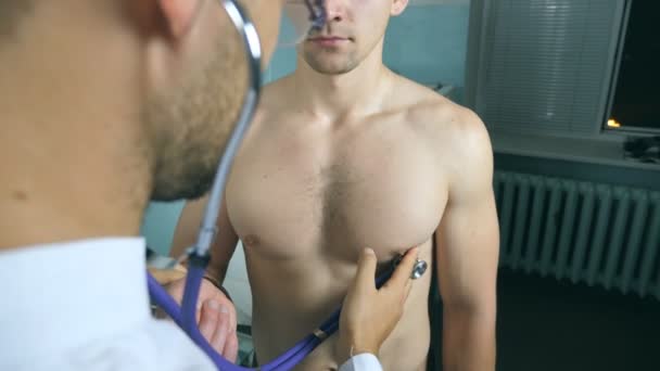 Ponto de vista do médico examinando jovem paciente do sexo masculino com estetoscópio. Trabalhador médico ouvindo batimento cardíaco de homem atlético. Médico a verificar a caixa de um tipo no consultório dela no hospital. Fechar POV — Vídeo de Stock