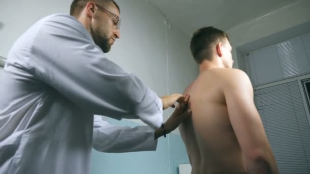 Médico comprobando la espalda de un tipo en su oficina en el hospital. Doctor examinando a un paciente joven con estetoscopio. Trabajador médico escuchando el latido del corazón del atleta. De cerca. — Vídeos de Stock