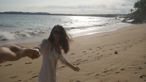 Sígueme la foto de una mujer joven tirando de su novio en la orilla del mar. Chica sosteniendo la mano masculina y corriendo en la playa tropical exótica al océano. Vacaciones de verano o vacaciones. Punto de vista. POV cámara lenta — Vídeos de Stock