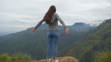 Dağ ve yükseltilmiş elleri yukarı ulaşan genç kız. Güzel Kanyon kenarında duran, zaferle yukarı silah outstretching kadın turist. Ağır çekim arka geri görüntülemek