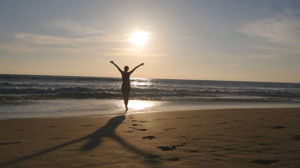 Junge Frau läuft am Strand zum Meer bei Sonnenuntergang und hebt die Hände. schönes junges Mädchen, das am Sandstrand zum Meer geht und im Urlaub die Freiheit genießt. Entspannung im Sommerurlaub. Rückansicht — Stockfoto