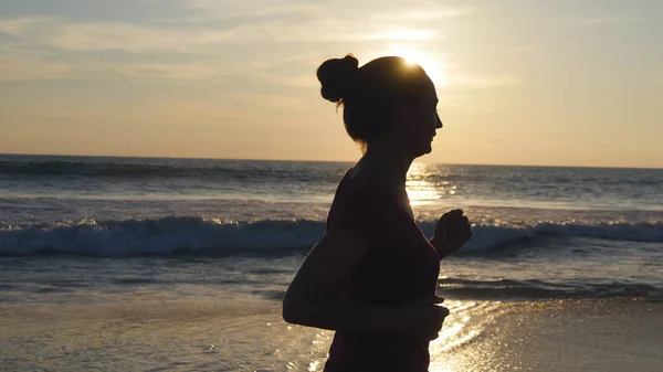 Σιλουέτα της νεαρής γυναίκας που τρέχει στην παραλία το ηλιοβασίλεμα. Κορίτσι τζόκινγκ κατά μήκος της ακτής του ωκεανού κατά την Ανατολή του ηλίου. Θηλυκά αθλητής ασκούν εξωτερική. Τρόπος ζωής υγιή ενεργό προπόνηση στη φύση. Κοντινό πλάνο — Φωτογραφία Αρχείου
