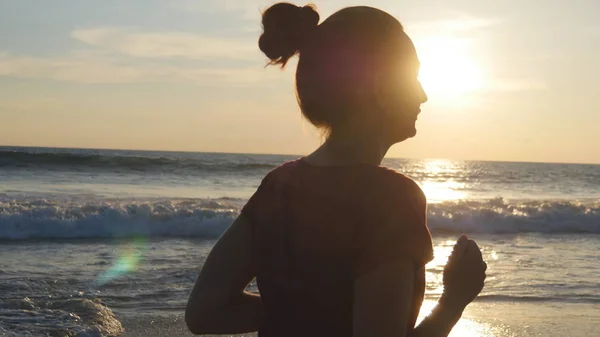 Sylwetka młoda kobieta działa na plaży o zachodzie słońca. Dziewczynka jogging wzdłuż brzegu oceanu podczas sunrise. Ćwiczeń odkryty kobiece sportowca. Styl życia zdrowy treningu o charakterze. Z bliska — Zdjęcie stockowe