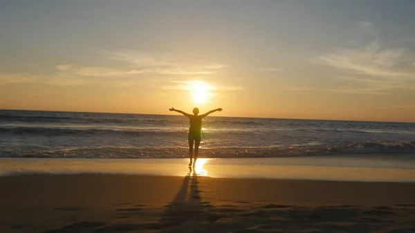 Junge Touristin mit Rucksack am Strand zum Meer bei Sonnenuntergang und erhobenen Händen. Wanderin, die an der Sandküste bis zum Meer wandert und in den Sommerferien die Freiheit genießt. Rückansicht — Stockfoto