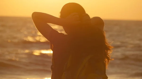 Junge Touristin bindet Pferdeschwanz am Strand in der Nähe des Meeres bei Sonnenuntergang. schöne Mädchen pressen ihre Haare am Meeresufer bei Sonnenaufgang. Backpacker flechten Haare und machen Frisuren. Haarpflege Rückansicht — Stockfoto