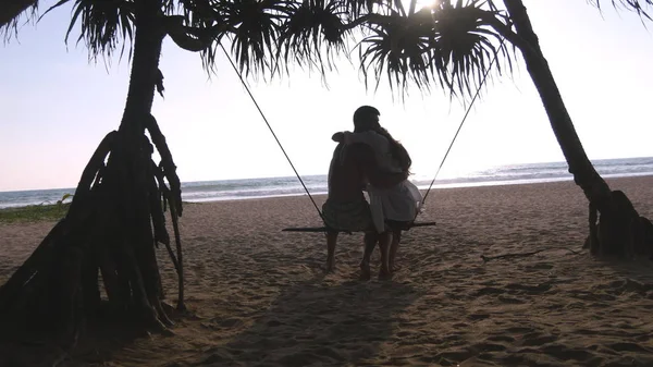 Giovane coppia romantica seduti insieme su altalena sulla spiaggia tropicale del mare e abbracci. Coppia innamorata rilassante e baciarsi sulla riva esotica dell'oceano durante le vacanze estive. Concetto vacanza Indietro vista posteriore — Foto Stock