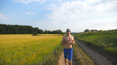 Ülke Road'da koşan kaslı adam. Alan üzerinde kırsal iz koşu genç atletik bir adam. Erkek sporcu doğa eğitim. Runner açık egzersiz. Sağlıklı aktif yaşam tarzı yakın çekim