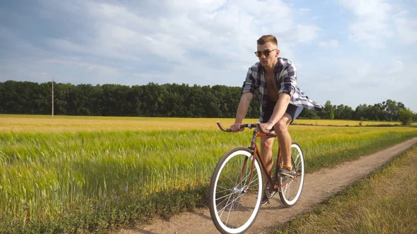 Sporty guy cycling along country trail outdoor. Young man riding vintage bicycle at the rural road over field. Male cyclist riding bike in the countryside. Healthy active lifestyle — Stock Photo, Image