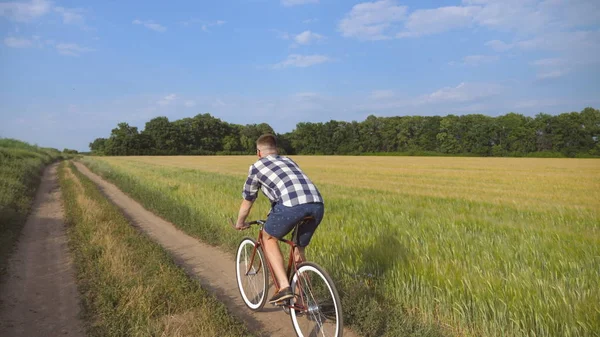 Junger Mann mit Oldtimer-Fahrrad auf der Landstraße über Feld. Sportlicher Typ, der auf Feldwegen im Freien radelt. Fahrradfahrer auf dem Land. Gesunder aktiver Lebensstil — Stockfoto