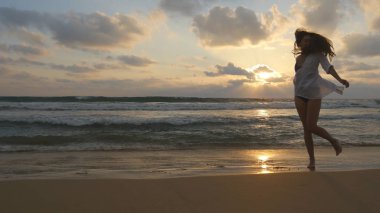 Okyanusa yakın sahilde koşan ve dönen mutlu kadın. Genç güzel kız yaşam zevk ve deniz kıyısında eğlenmek. Yaz tatili veya tatil. Arka planda günbatımı deniz manzara