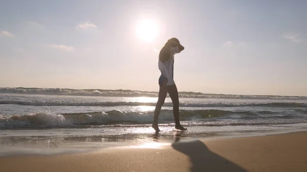 Happy Woman wandelen op het strand van de Oceaan en spuiten het water met haar voeten. Jong mooi meisje genieten van het leven en plezier hebben op zee kust. Zomervakantie. Landschap op de achtergrond. Close-up — Stockfoto