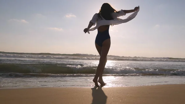 Щаслива жінка йде і крутиться на пляжі біля океану. Молода красива дівчина насолоджується життям і розважається на морському березі. Су — стокове фото