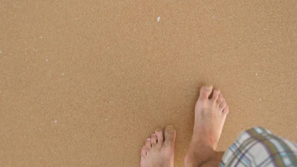 Punto de vista del joven pisando la arena dorada en la playa del mar. Piernas masculinas caminando cerca del océano. Pie desnudo de tipo que va en la orilla arenosa con olas. Vacaciones de verano o vacaciones Close up POV —  Fotos de Stock