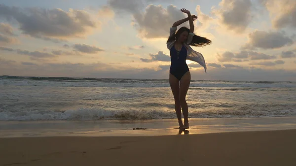 Lycklig kvinna promenerar på stranden av oceanen och sprutning vattnet med fötterna. Ung vacker flicka njuter av livet och att ha kul på havet. Sommarsemester. Solnedgång landskap i bakgrunden — Stockfoto