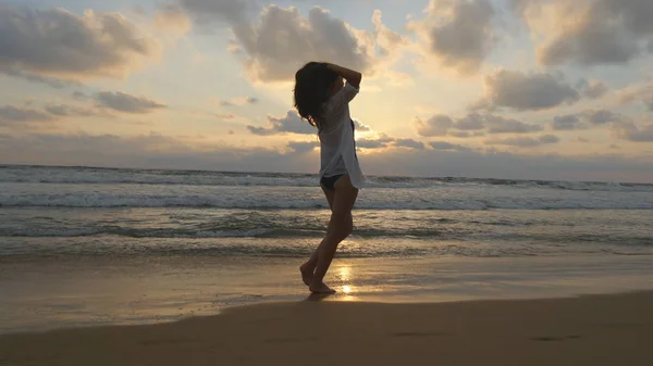 Ευτυχισμένη γυναίκα περπάτημα και γυρίζοντας στην παραλία κοντά στον ωκεανό. Όμορφη κοπέλα απολαμβάνοντας τη ζωή και τη διασκέδαση στο κύμα της θάλασσας. Ή καλοκαιρινές διακοπές. Τοπίου ηλιοβασίλεμα στο φόντο, κοντινό πλάνο — Φωτογραφία Αρχείου