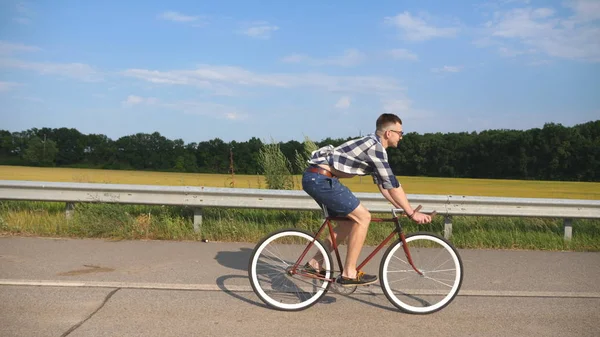 Young handsome man riding at vintage bicycle in the country road. Sporty guy cycling at the track. Male cyclist riding fixed gear bike at highway. Healthy active lifestyle Slow motion — Stock Photo, Image