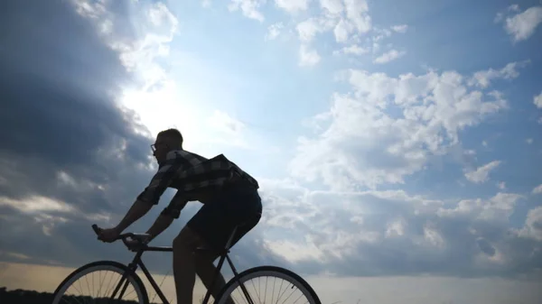 Silhueta de jovem andando de bicicleta vintage com belo céu pôr do sol no fundo. Um tipo desportivo a andar de bicicleta na estrada do campo. Bicicleta de ciclista masculino. Estilo de vida ativo saudável Movimento lento — Fotografia de Stock