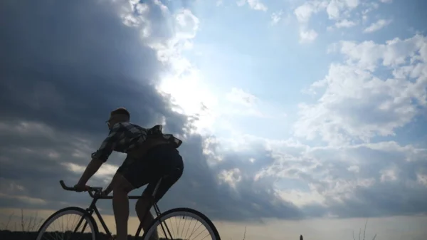 Silhouette of young man riding at vintage bicycle with beautiful sunset sky at background . Sporty guy cycling in the country road. Male cyclist riding bike. Healthy active lifestyle Slow motion — Stock Photo, Image