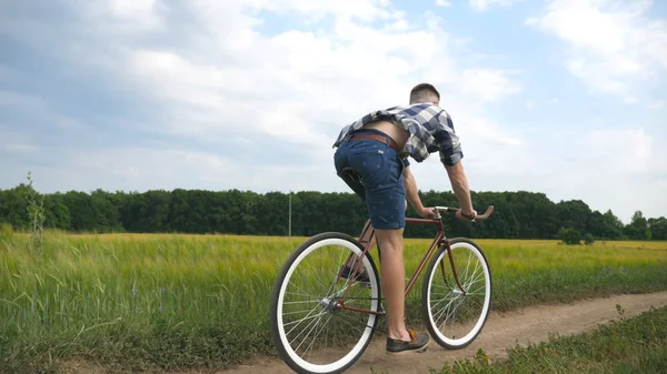 Junger Mann mit Oldtimer-Fahrrad auf der Landstraße über Feld. Sportlicher Typ radelt auf Feldwegen im Freien. Männliche Fahrradfahrer auf dem Land. Gesunder aktiver Lebensstil Zeitlupe — Stockfoto