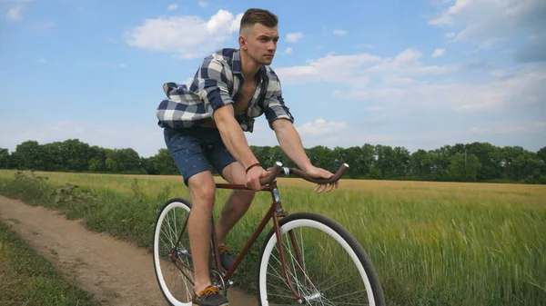 Jovem andando de bicicleta vintage na estrada rural sobre o campo. Sporty guy ciclismo ao longo da trilha country ao ar livre. Ciclista do sexo masculino andar de bicicleta no campo. Estilo de vida ativo saudável Movimento lento — Fotografia de Stock